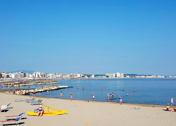 Beach with swimmers, umbrellas, and city in the background.